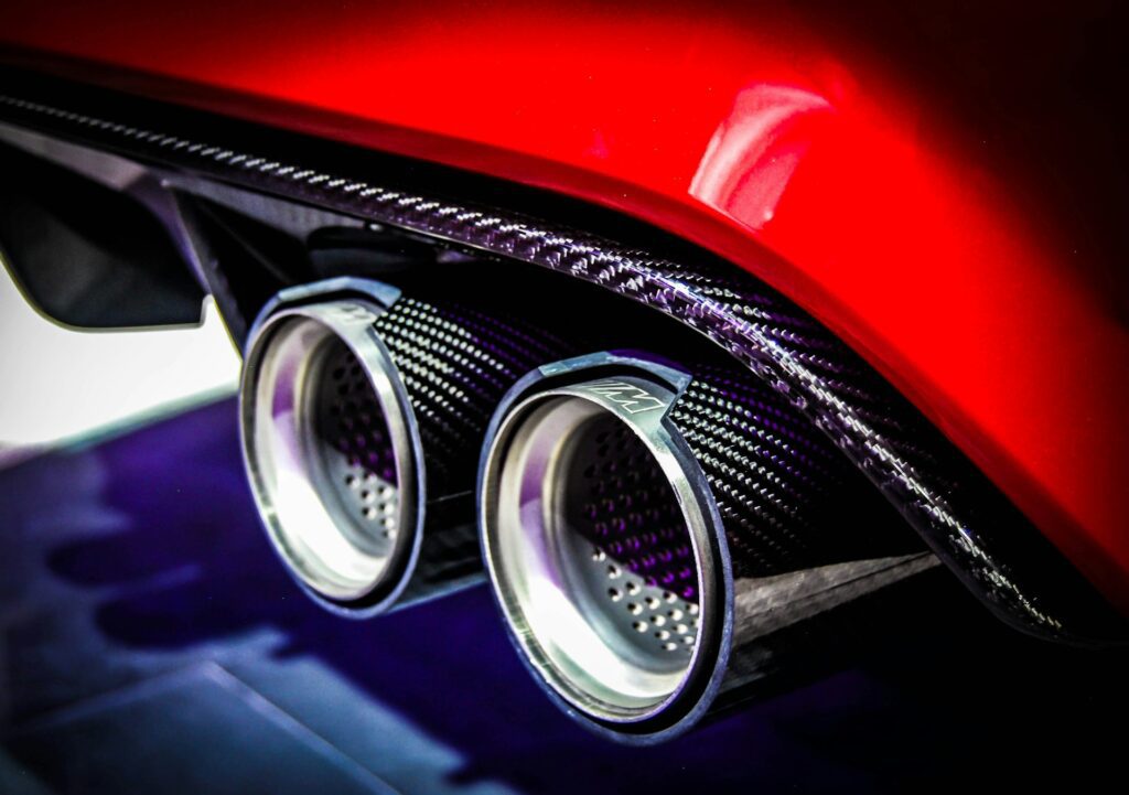 Close-up of two sleek metallic exhaust pipes on a red sports car, showcasing intricate carbon fiber detailing.