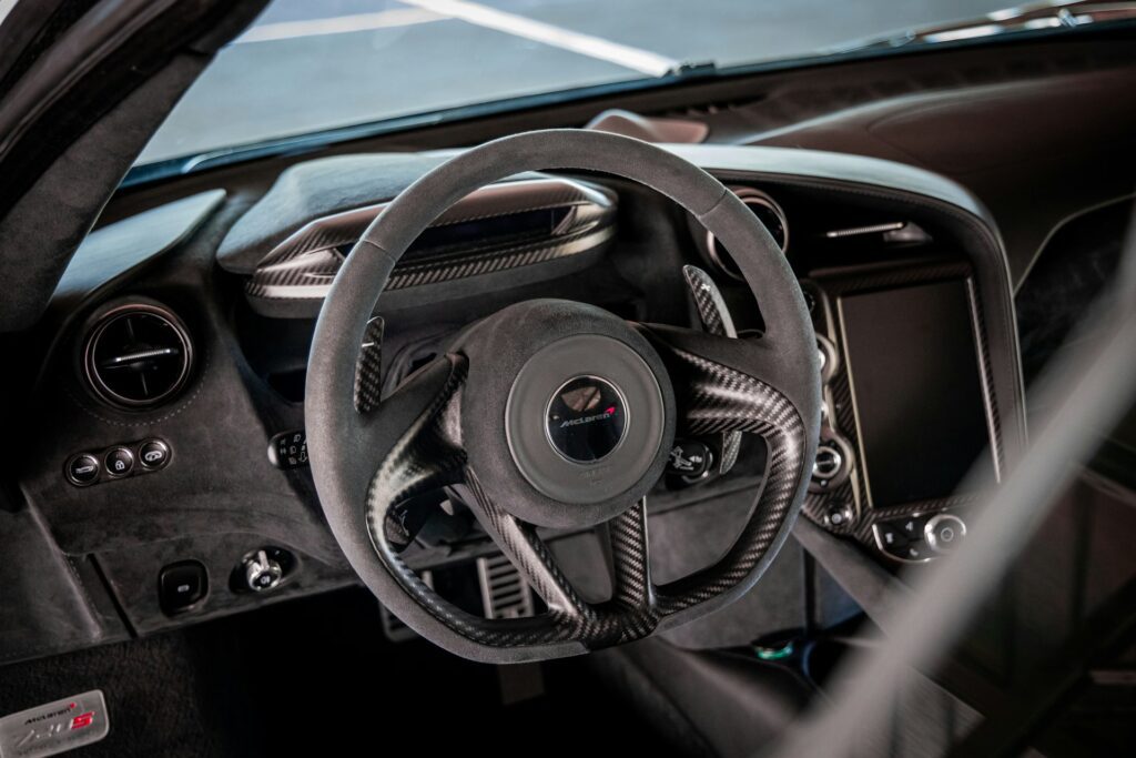 Close-up of a sports car steering wheel with a sleek carbon fiber finish and a vibrant digital dashboard in the background.